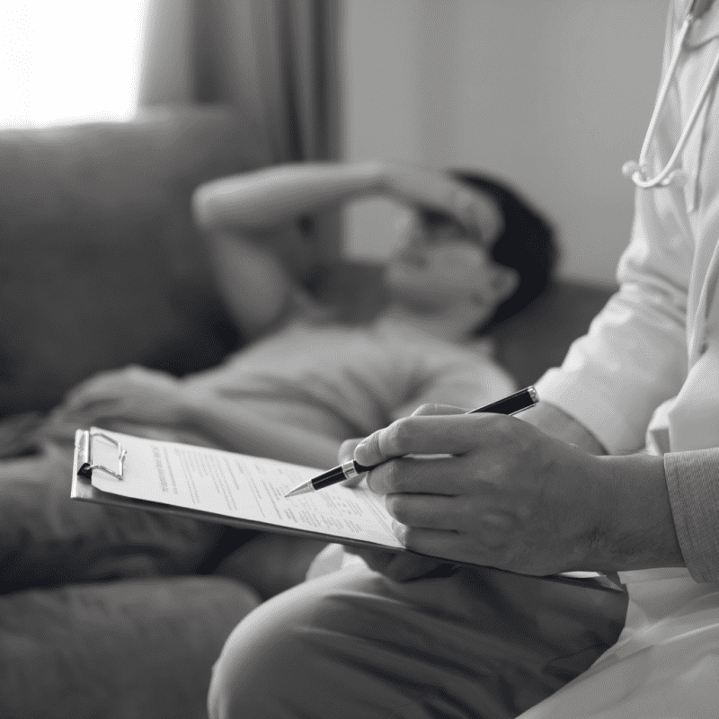 doctor looking at chart while patient touches forehead and the background